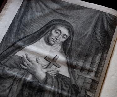 Detail of a printed book shows an illustration of a nun holding a cross to her chest.