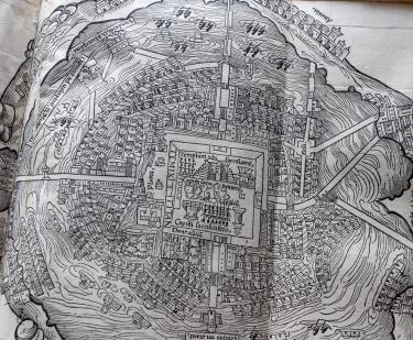 Detail of a fold-out printed map shows town square in the center, surrounding buildings, and ships at sea at the outer perimeter.